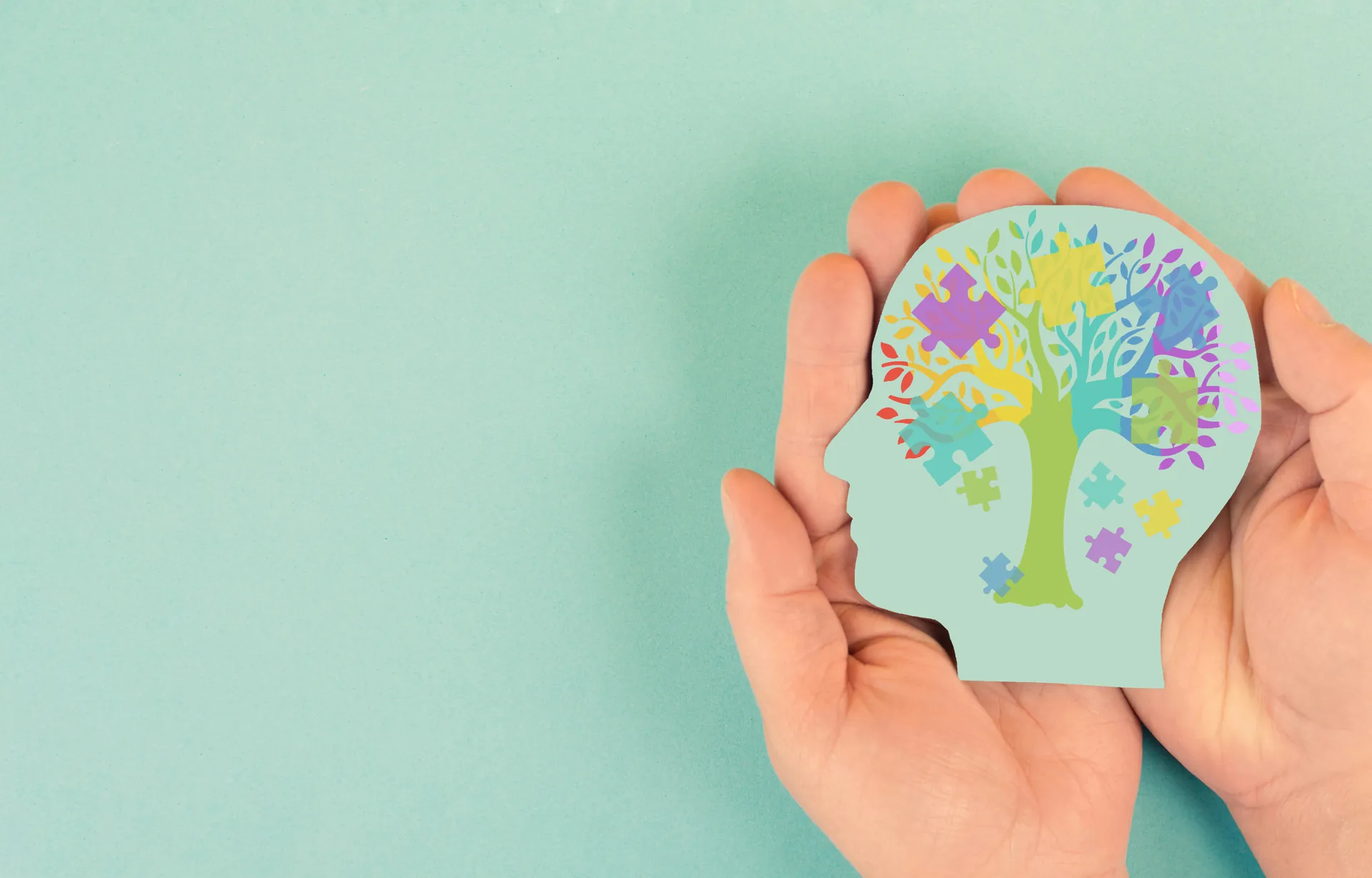 Hände halten die Silhouette eines Kopfes mit einem farbigen Puzzlebaum