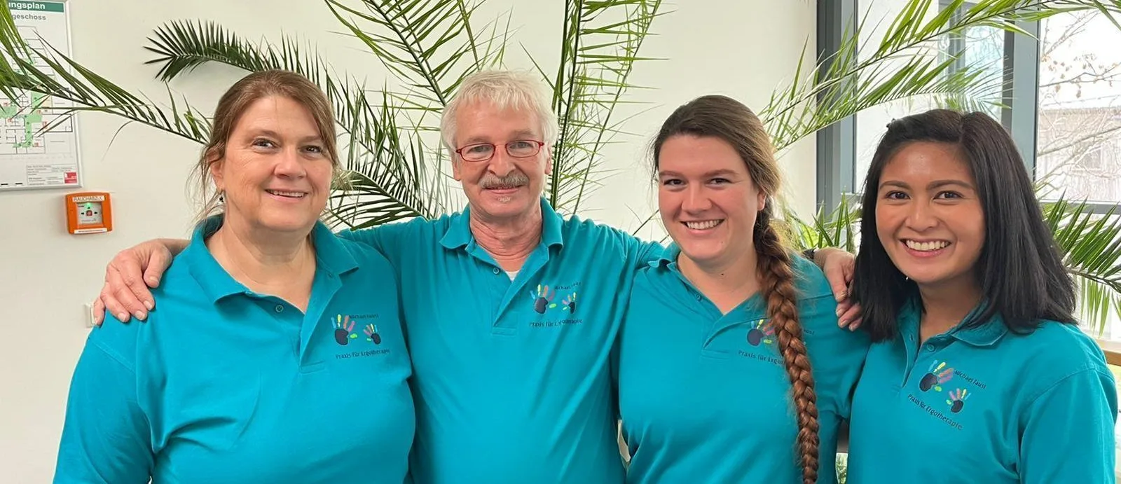 Das vierköpfige Praxisteam in türkisen Poloshirts vor einer Zimmerpflanze